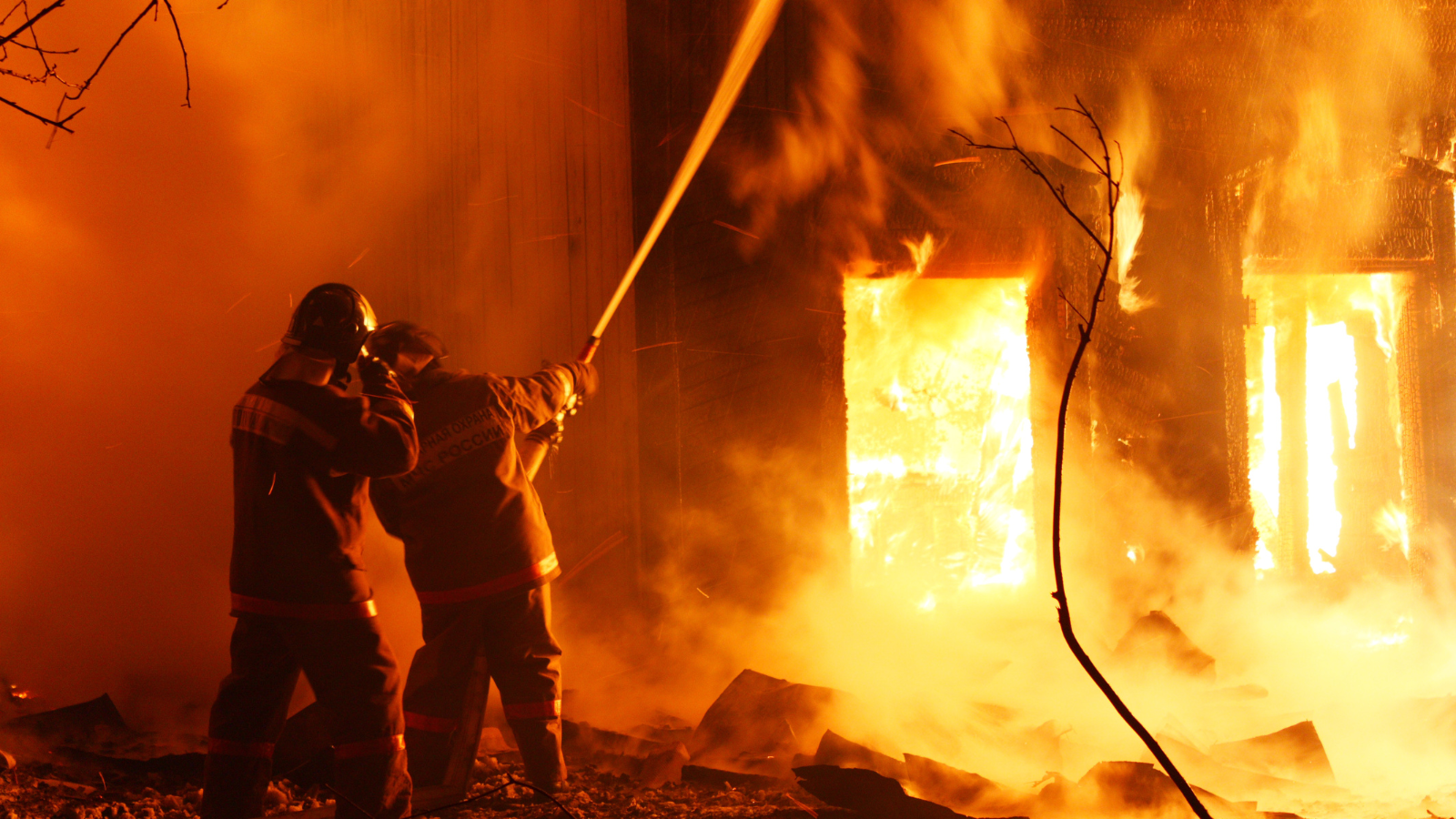 two firefighters holding water hose spraying in burning house